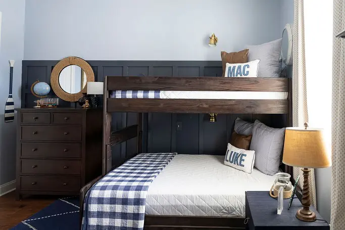 A navy and white-themed bunk bed room with wooden paneling. Personalized pillows with names, a large dresser, and vintage nautical decor complete the classic, timeless look.
(@morgankrulisky).