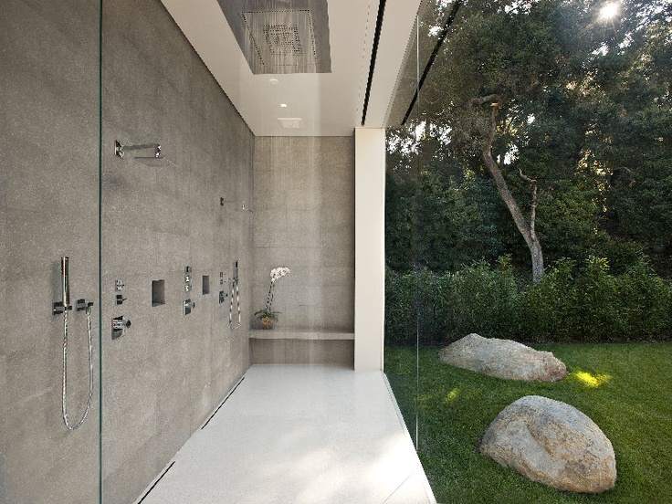 An indoor shower space done with concrete, with a clear glass wlal that lets the homeowners enjoy the views of their private garden.