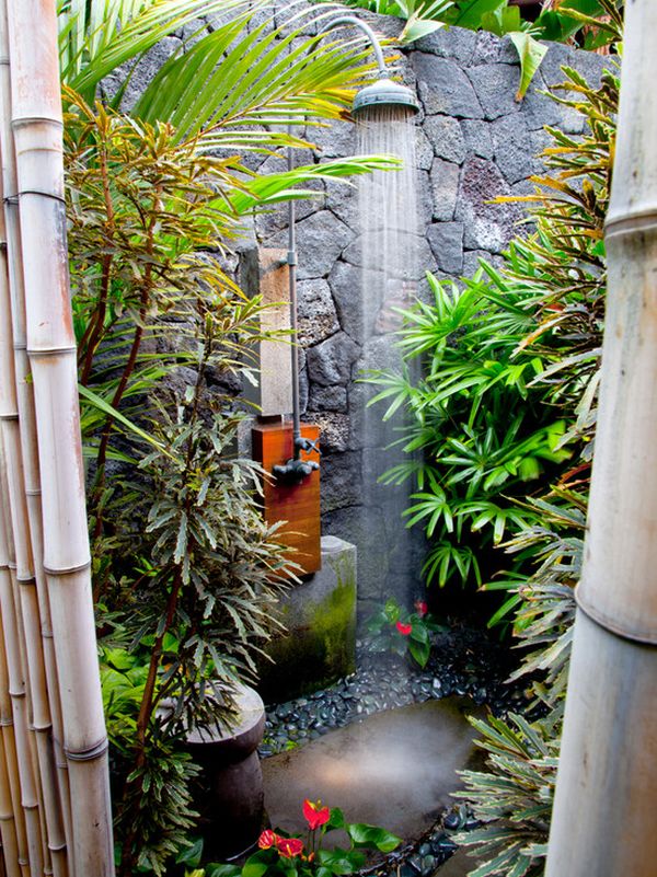 An outdoor tropical shower space with a stone wall and stones on the ground, tropical plants and a rain shower is a lovely idea.