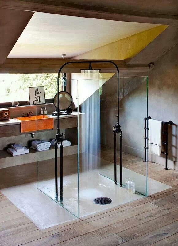 A creative attic shower space enclosed in glass, with a black shower head, with a small window to enjoy natural light.