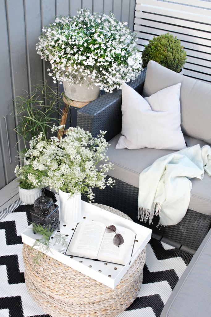 A summer Scandinavian terrace in black and white, with dark furniture, blooms and greenery in pots and a cool ottoman.