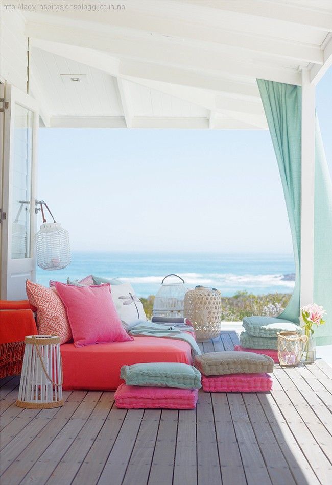 A colorful summer seaside terrace with a bright daybed, colorful pillows and cushions and candle lanterns.