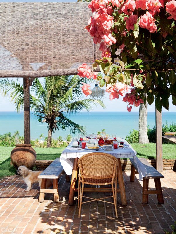 A bright summer terrace with lots of blooms and palm trees, with wooden furniture and rattan chairs, with a gorgeous sea view.