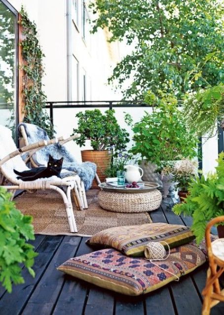 A bright boho summer terrace with rattan chairs, a wicker ottoman, potted greenery, a jute rug and boho pillows.