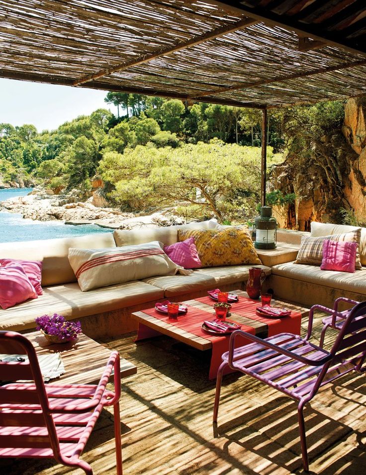 A bright and colorful terrace with neutral upholstered benches, colorful pillows, bright stools and textiles plus a sea view.