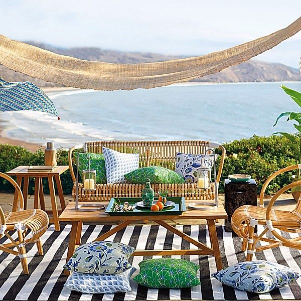 A bright and bold summer terrace with a cool sea view, a striped rug, rattan furniture, colorful textiles is super welcoming.