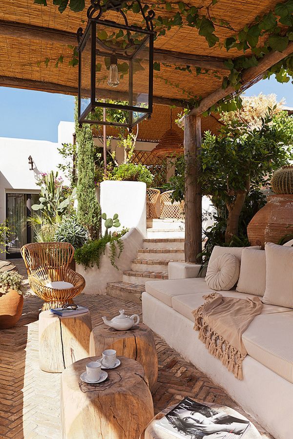 A neutral Mediterranean terrace with neutral furniture, wooden tables, a rattan chair and lots of greenery around.