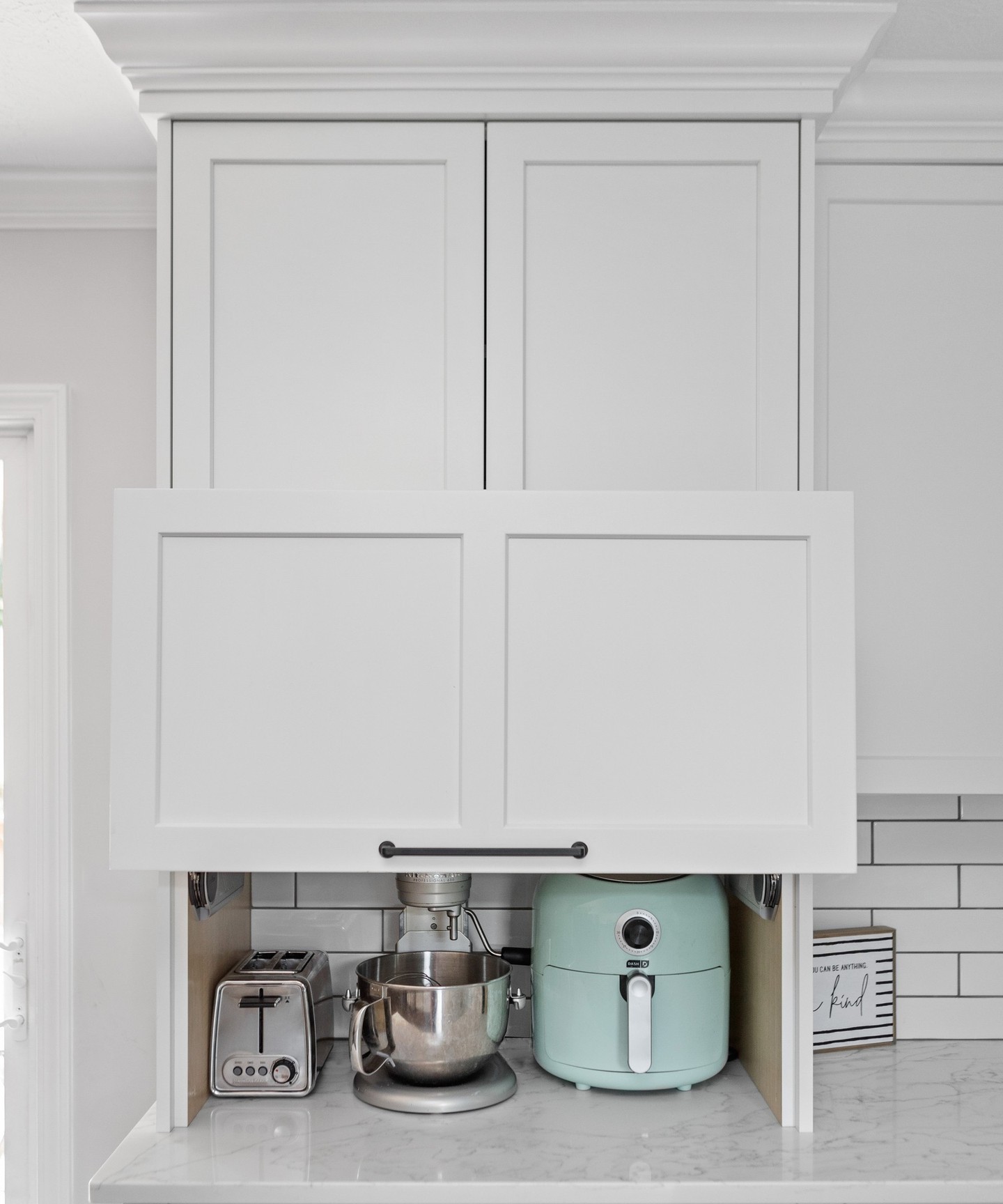 A stylish lift-up door conceals a range of small appliances, including a stand mixer, air fryer, and toaster, keeping the kitchen looking seamless. The white cabinetry blends with the marble countertop, ensuring a clean and organized aesthetic.

(@durasupreme).