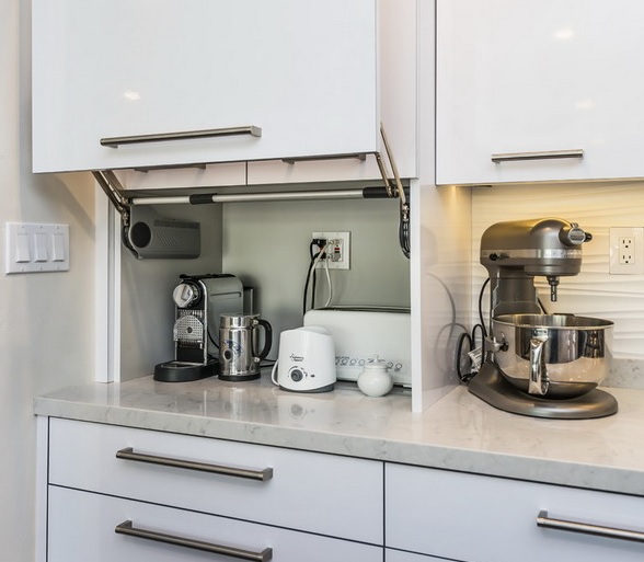 A white cabinet with a coffee machine, a kettle, a toaster and some other appliances is a cool idea to store your stuff without cluttering the space.