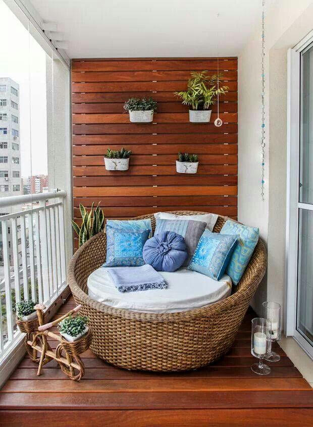 A contemporary balcony clad with stained wood, with a wicker chair, potted greenery and succulents and bright textiles.