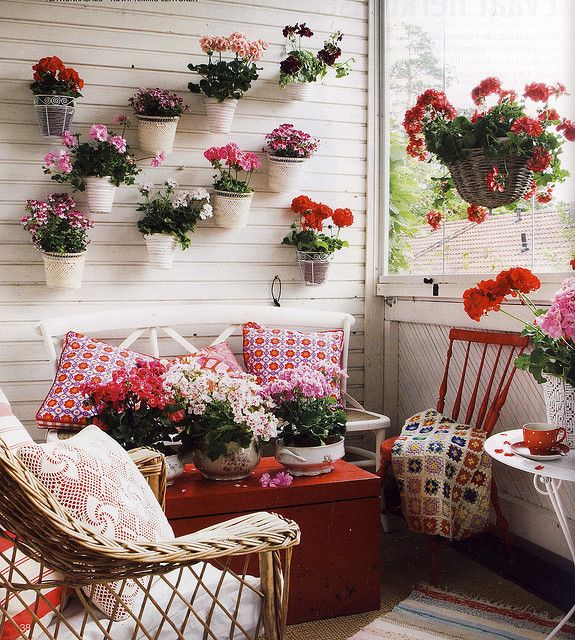 A super bright vintage balcony in white, with lots of red, potted blooms and greenery and bright printed textiles for a bold look.
