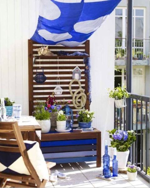 A seaside inspired summer balcony with blue textiles, a painted bench, potted blooms, blue bottles and pillows.