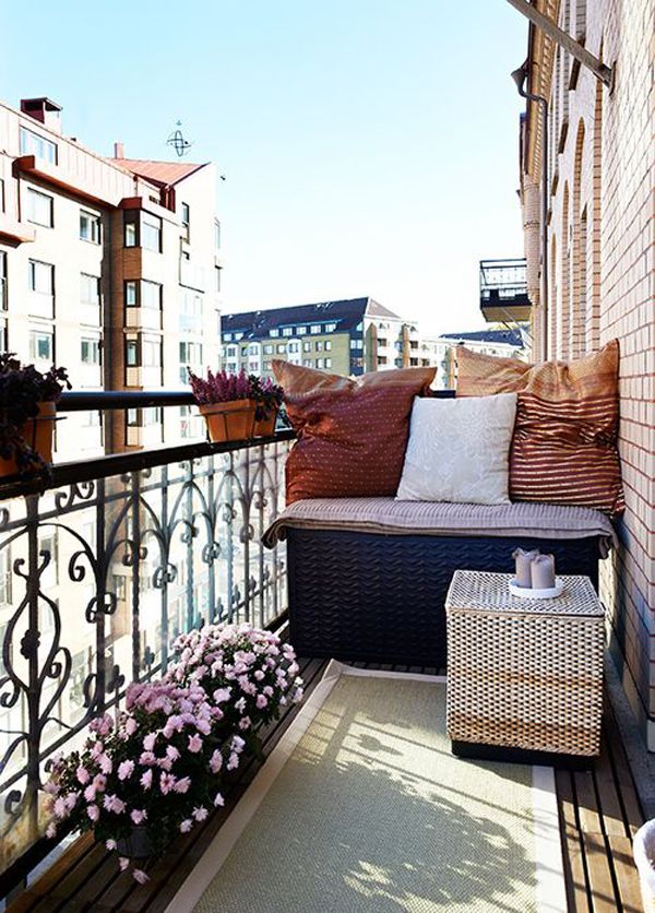 A bright summer balcony with wicker furniture, potted blooms and colorful textiles looks cute and very inviting.