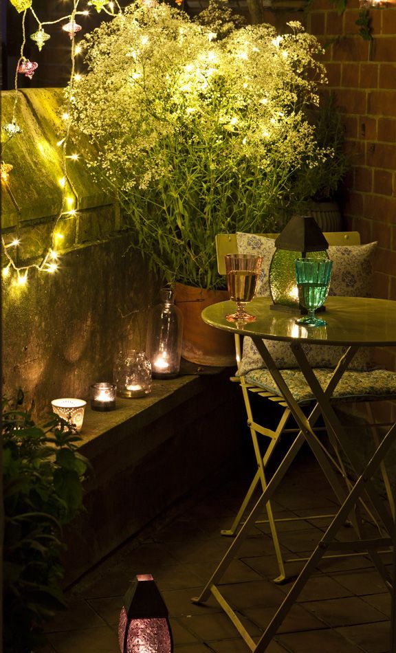 Simple summer balcony decor with potted greenery and blooms, with candles and lights and vintage metal furniture.