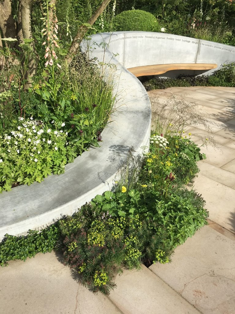 This contemporary garden is done with a curved concrete bench and greenery around. The bench goes along the whole garden bed.