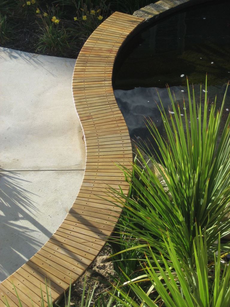 The contemporary water feature is curved and there's a wooden bench on top of it.