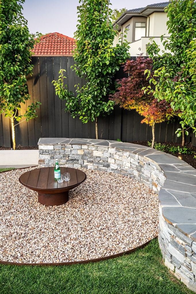 The round patio is styled with gravel and the curved stone bench adds style and a trendy feel here.