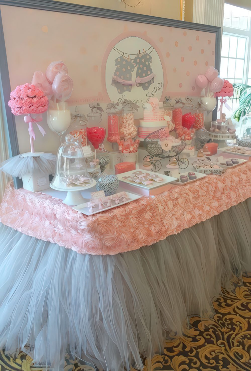 A grey and pink dessert table with tulle, fabric roses, fake floral arrangements and a polka dot backdrop.