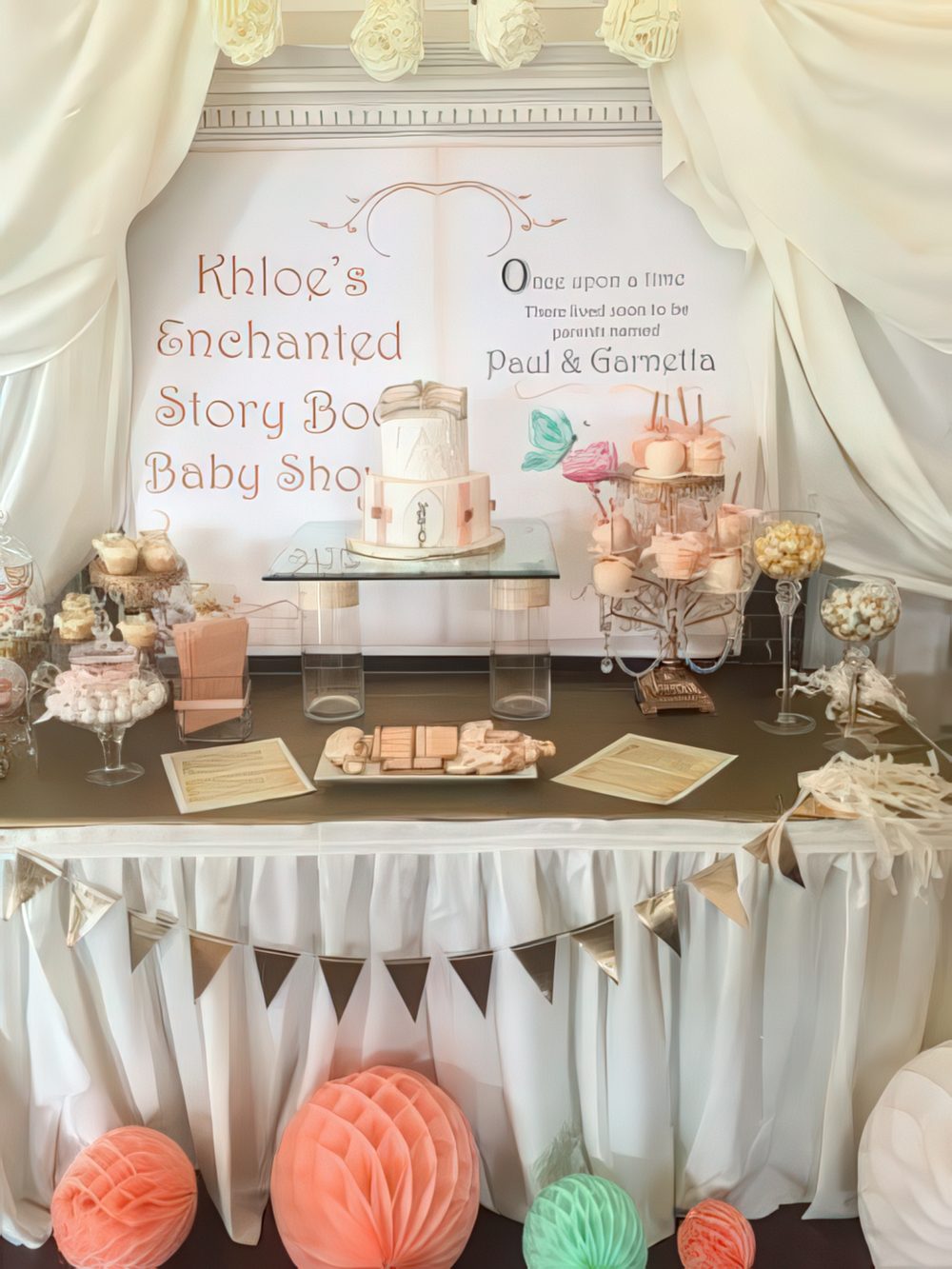 A gender neutral dessert table done in mint and coral, with a framed sign showing a story book and curtains.