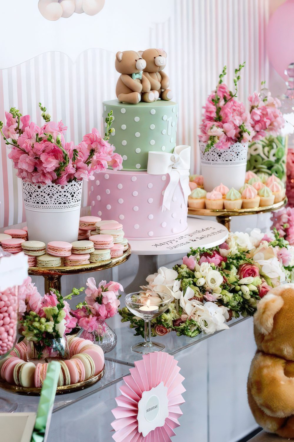 A bright pink and green baby shower with bright florla arrangements, colorful macarons and a cute two color cake with teddy bears.