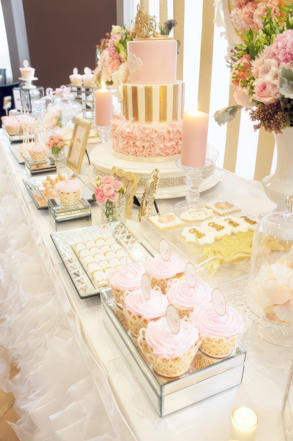A girlish pink and gold dessert table with stripes, ruffles, candles and gold frames for a girl's baby shower.