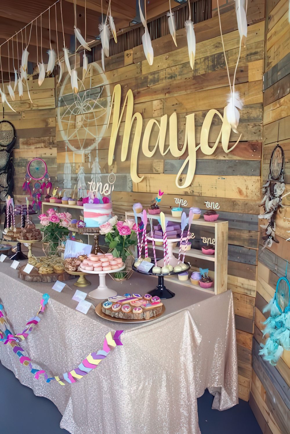 A super colorful dessert table done with purple, pink and turquoise touches, feathers, garlands and a dream catcher for a boho feel.