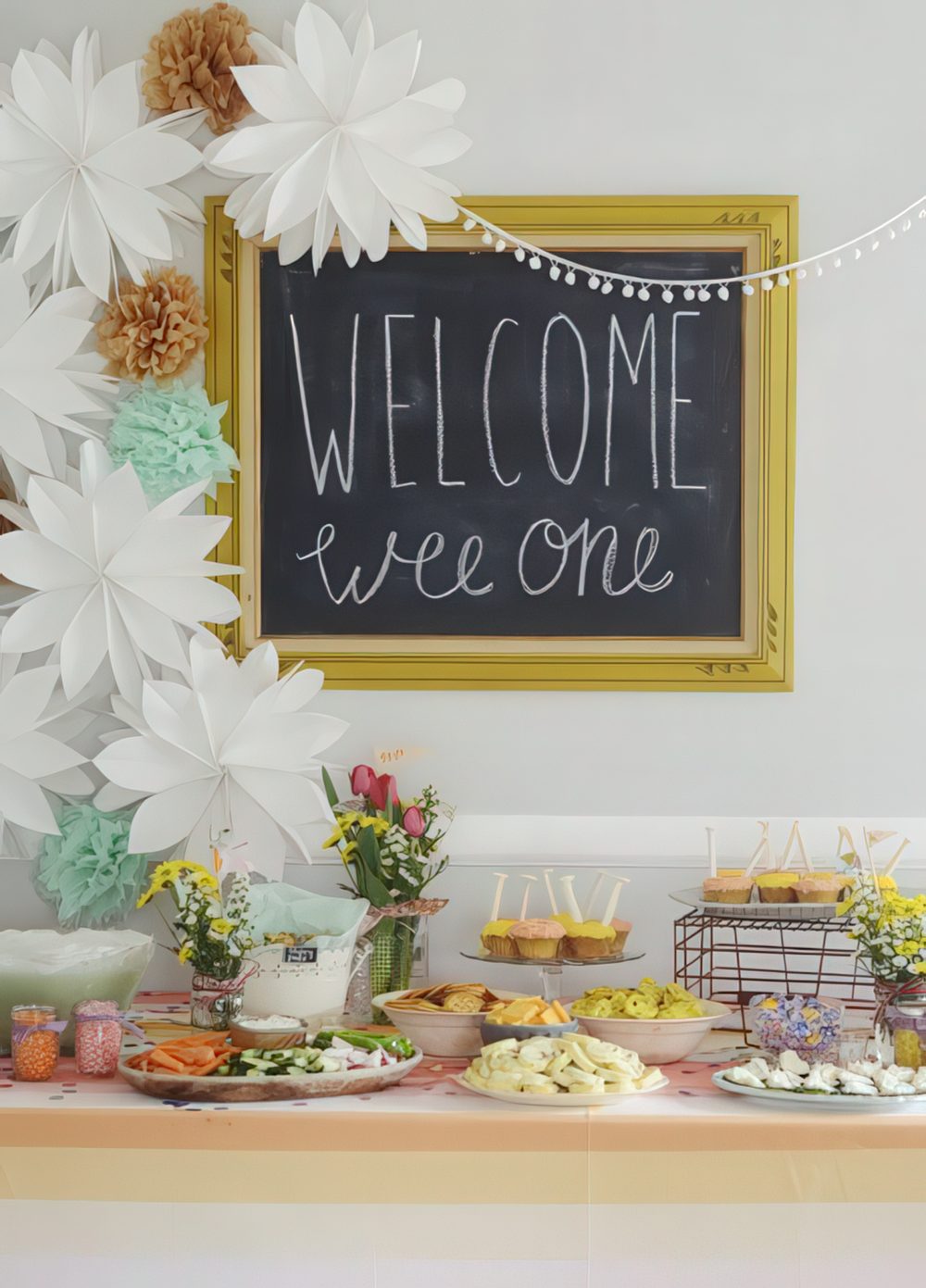 A bright dessert table styled with a framed chalkboard sign, paper flowers and pompoms and simple wildflower centerpieces.