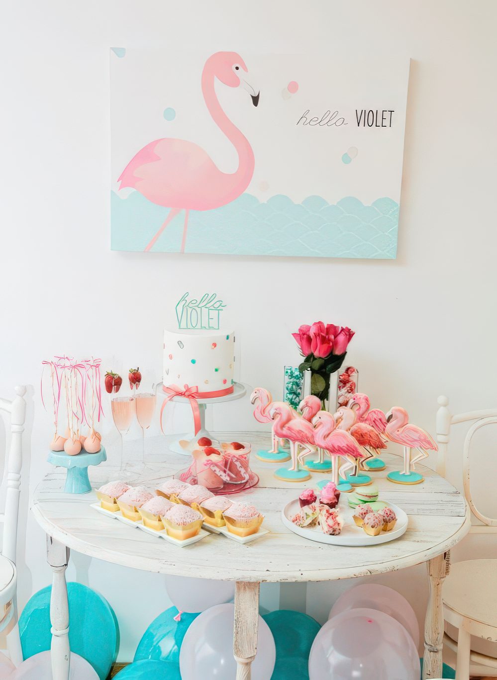 A colorful aqua and pink dessert table with flamingos, pink roses, a polka dot cake and a flamingo art piece.