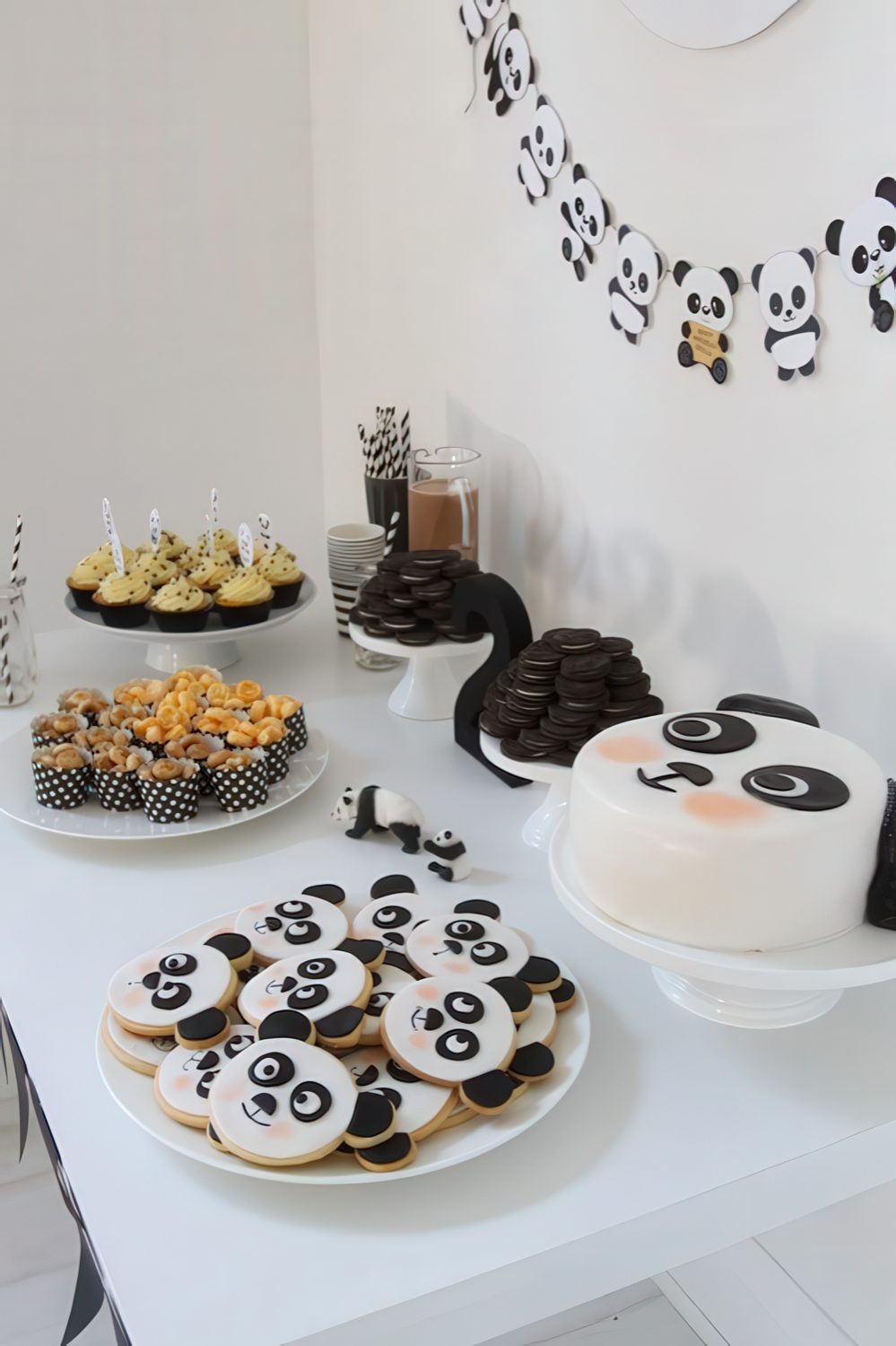 A fun panda-inspired dessert table with a panda banner, panda cookies and a cake plus some black and white sweets.