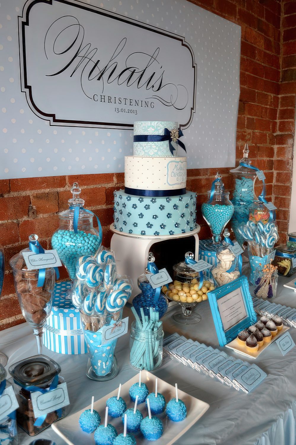 A turquoise and blue dessert table with lots of sweets displayed in jars, on plates, glasses and a large wedding cake on a stand.