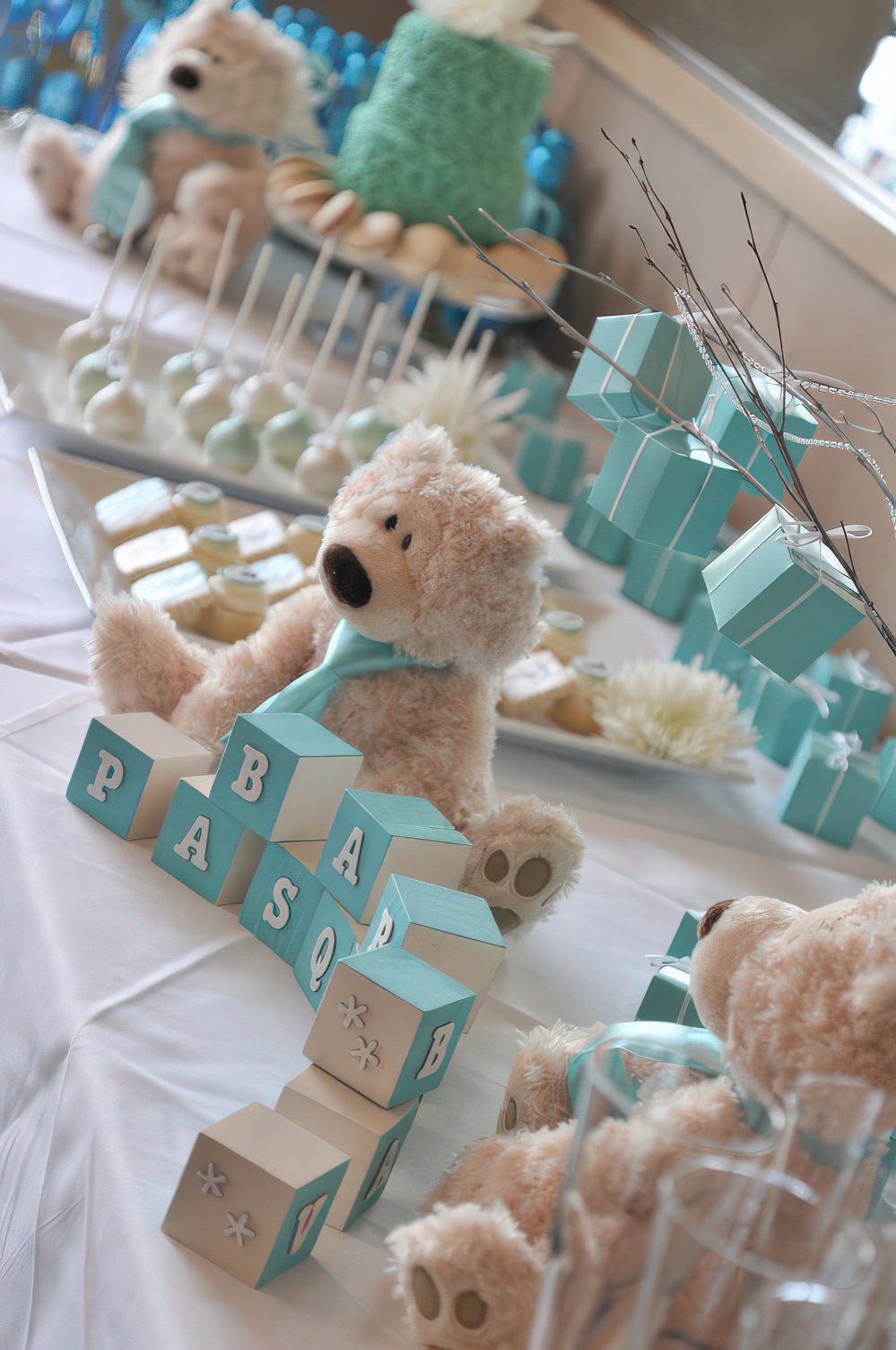 A boy's baby shower dessert table decorated in turquoise, with turquoise cubes and a funny teddy bear.