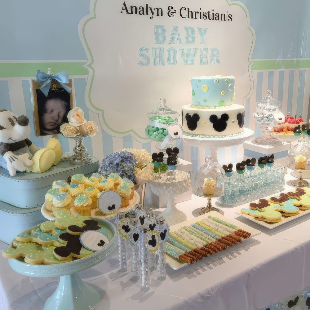 A gender neutral baby shower dessert table done in blue and green, with lots of Mickey Mouse desserts and decorations.