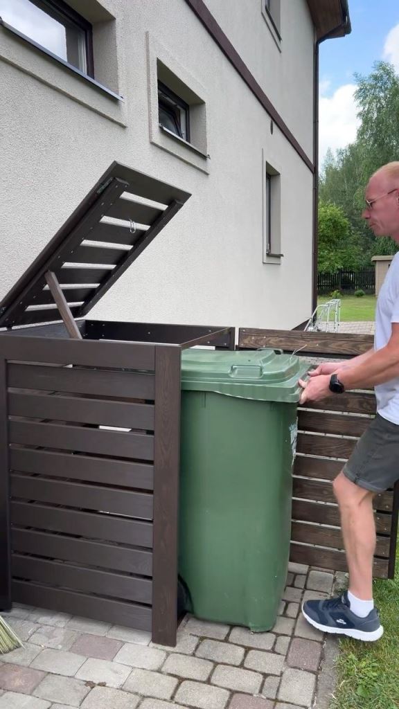 The dark-stained slatted box with a lid hides a single trash can and doesn't spoil the look of the facade.

(via instagram).