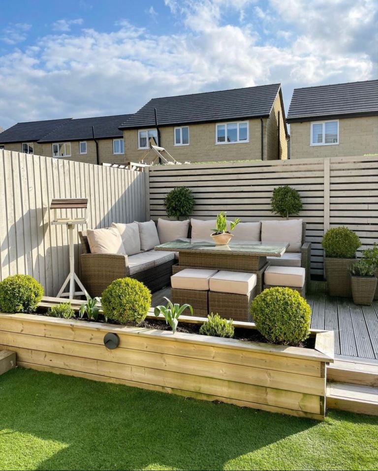 This small raised deck is placed in the corner at the fence, and wicker furniture and planters make up a nice modern space.