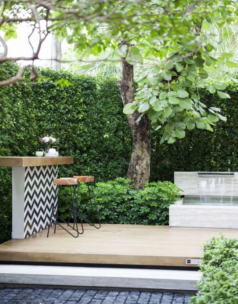 This long deck is placed at the living fence, and a large tree, greenery and a waterfall plus a bar counter make up a lovely contemporary space.