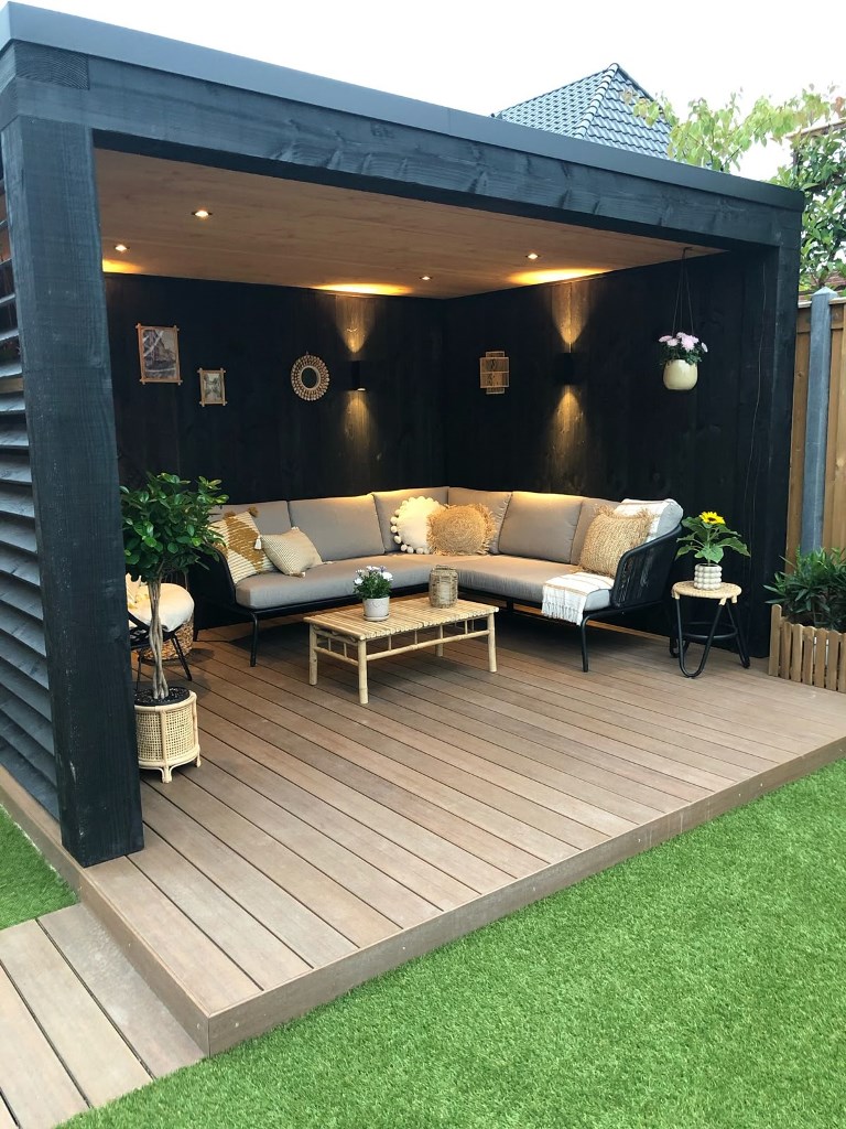 The deck with a black pergola with a solid roof is like an outdoor-indoor living room that is protected from the sun and rain.