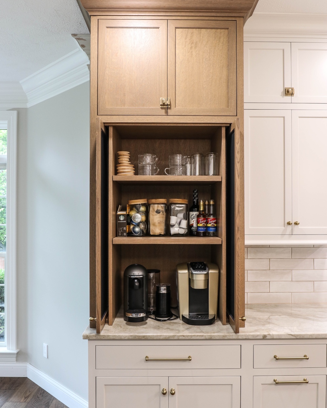 This warm-toned wooden coffee nook is discreetly tucked inside a pantry cabinet. With shelves for mugs, glassware, and coffee supplies, it offers a well-organized and elegant hideaway for caffeine lovers. (@gravellanedesign).