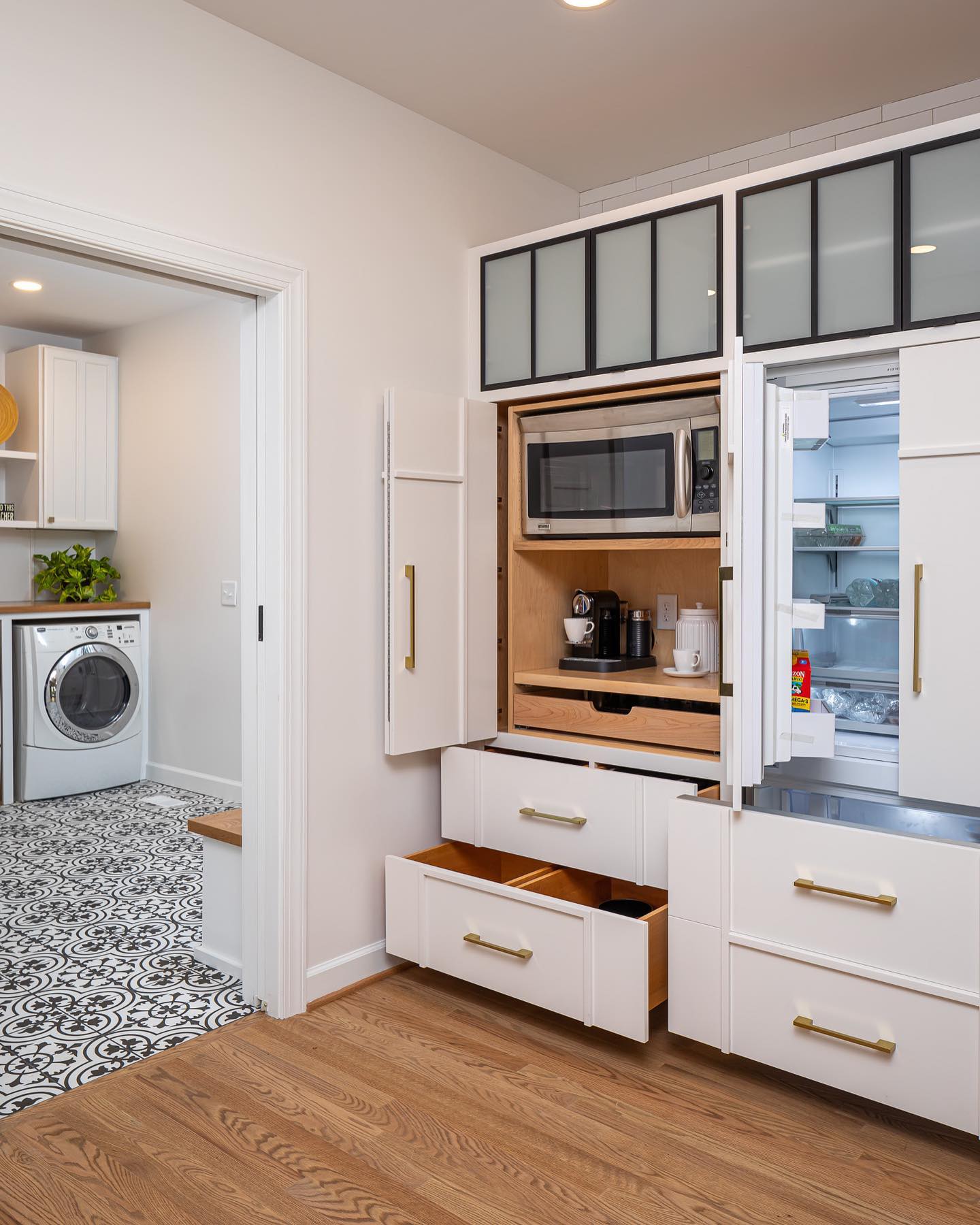 A built-in kitchen cabinet conceals a compact coffee and microwave station, creating a multifunctional space. The white shaker-style doors open fully, revealing a pull-out shelf for extra functionality. (@clearcutandco).
