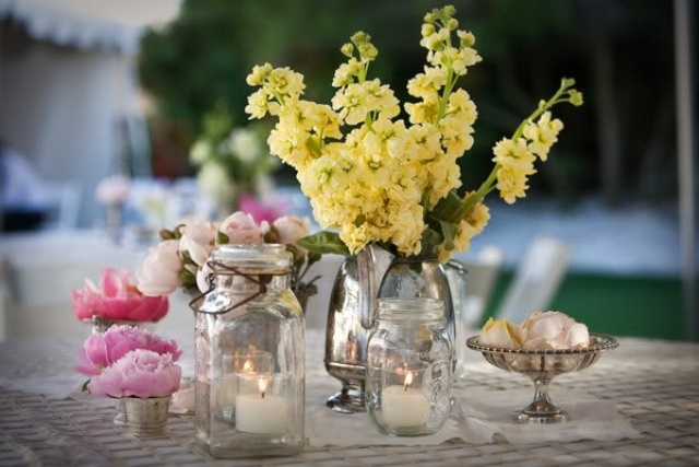 Jars and a vintage silver teapot with bright summer blooms and candles for a cool bright summer centerpiece.
