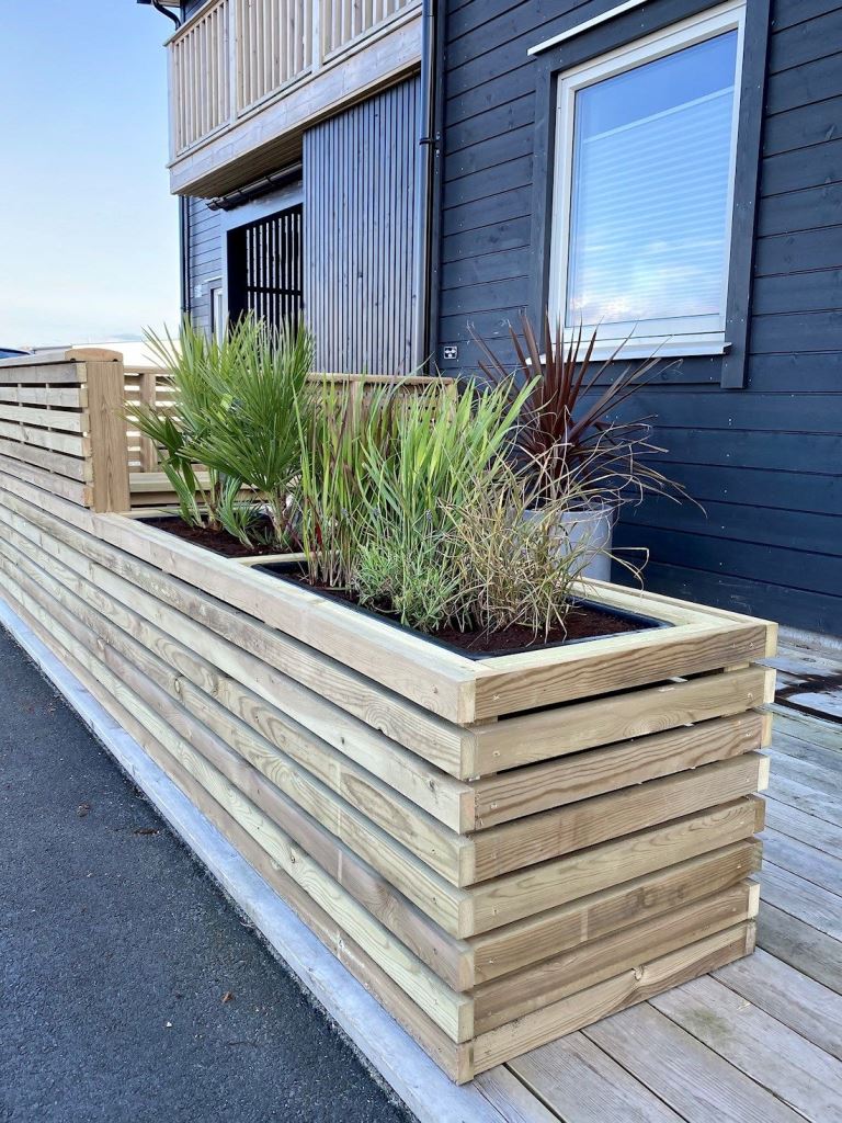 The deck is surrounded with slatted fence, which includes the planter with greenery.