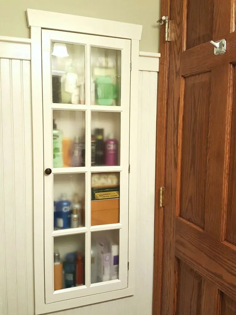 The built-in niche behind the door is turned into a closed storage unit with a glass door.