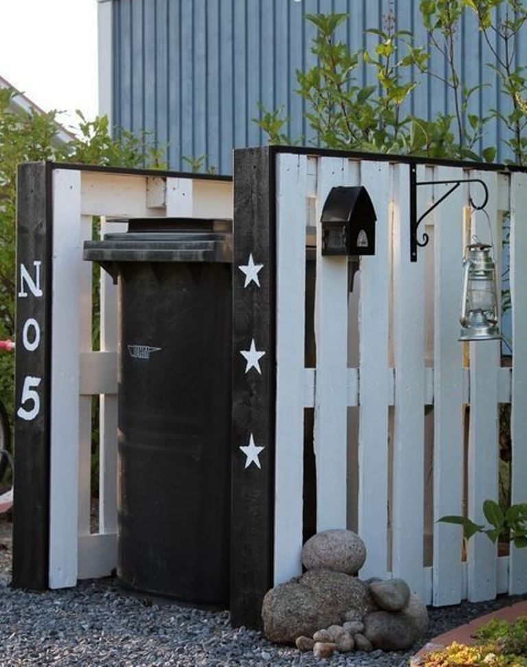 The trash can is covered with two pallets painted chalkboard and white, with the number of the house and a birdhouse and lantern attached.