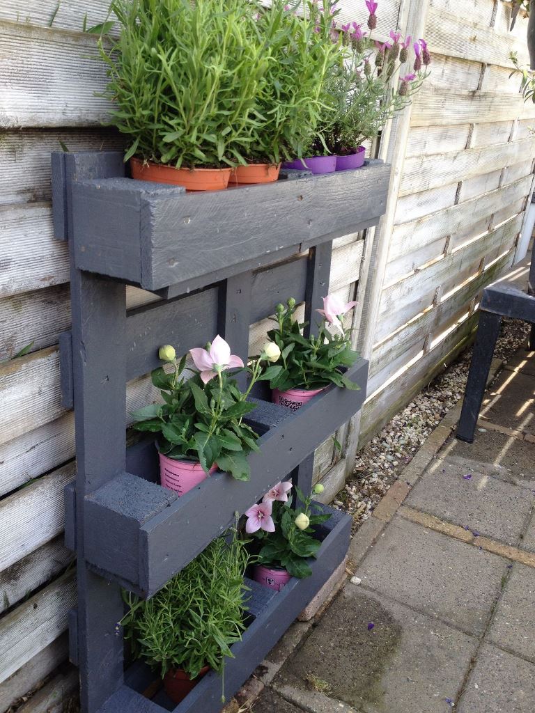 The graphite grey pallet holds potted blooms and greenery and it's a lovely solution for a relaxed rustic garden.