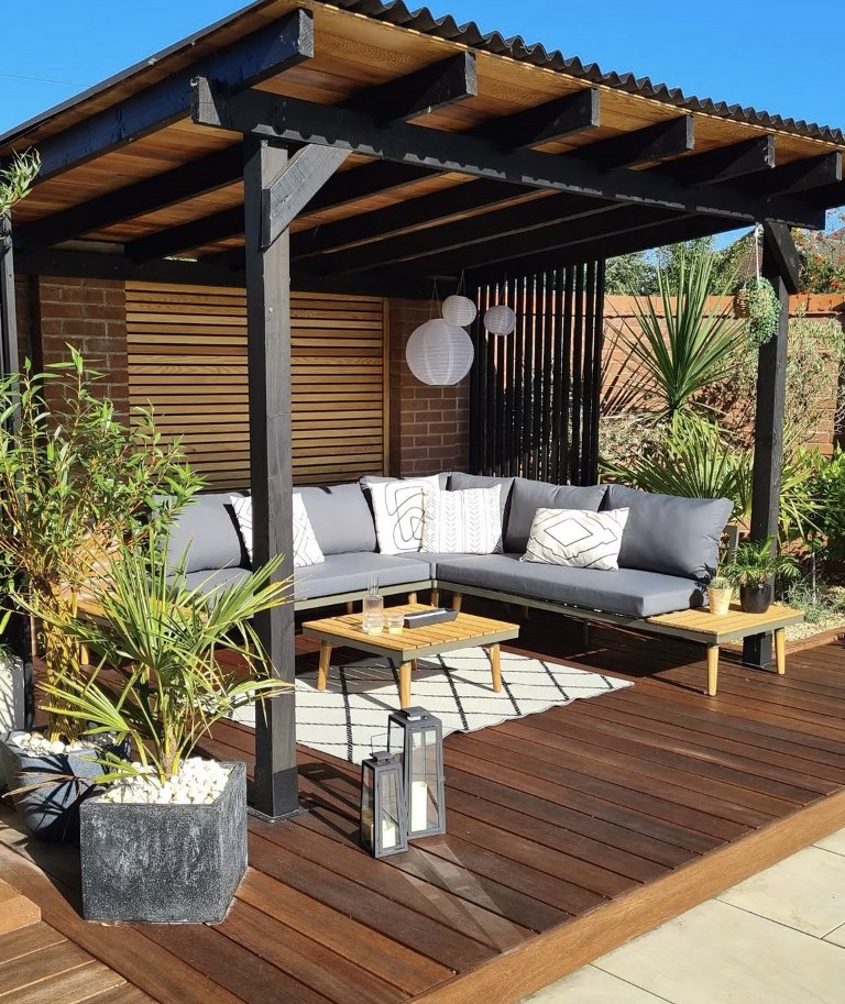 The stained raised deck with a pergola and a solid roof is great as an additional living room, and plants around make it feel more outdoorsy.