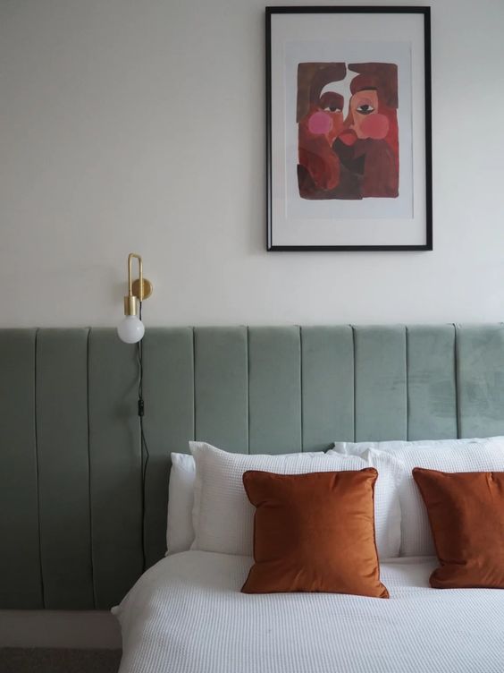 The bedroom shows off a sage green upholstered headboard, a gold sconce and a bold artwork.