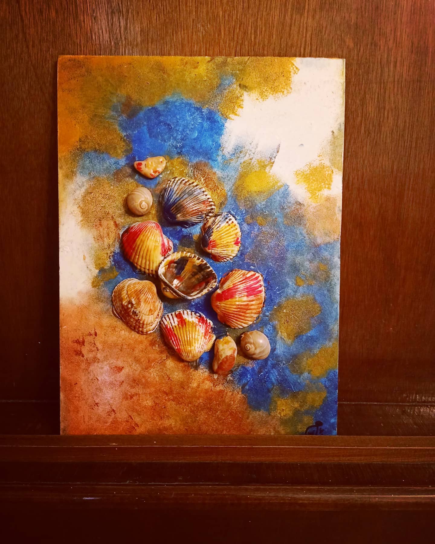 A vibrant wall canvas featuring real seashells blended into blue and sand-toned textures, evoking the colors and feel of the seashore.

(@forsha_alwan).