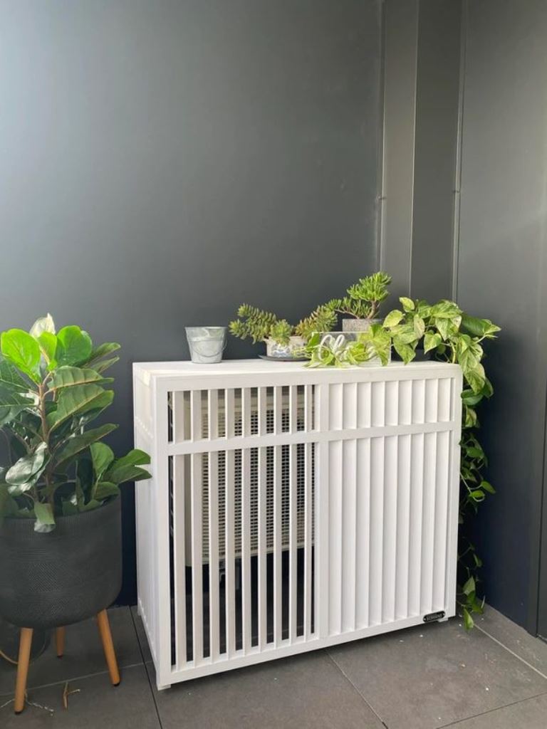 The AC unit is hidden inside a simple white slatted box, which is a plant stand at the same time.