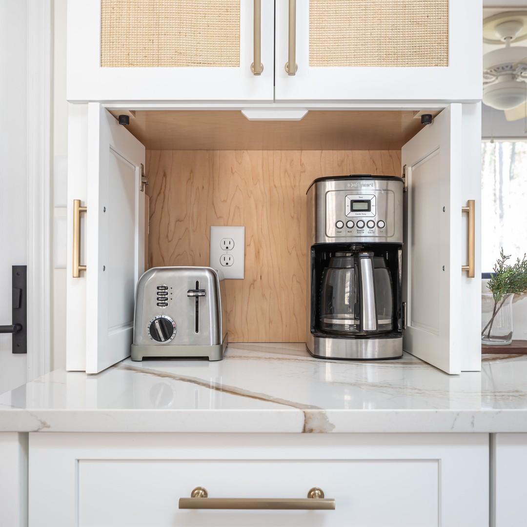 This clean and minimalist kitchen hides a coffee maker and toaster inside a custom white cabinet with woven rattan detailing. The natural wood interior adds warmth and charm while keeping appliances easily accessible. (@clearcutandco).