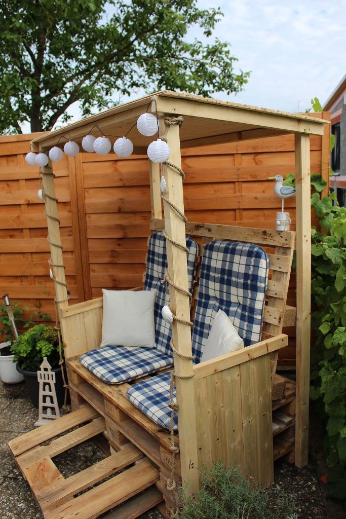 This small and cozy arbor is built of pallets and usual wood, with printed cushions and pillows and some lights over the space.