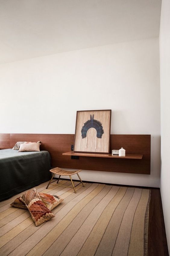 The chic bedroom shows off a bed with a wall-mounted rich-stained hanging headboard, with a vanity attached and a stool.